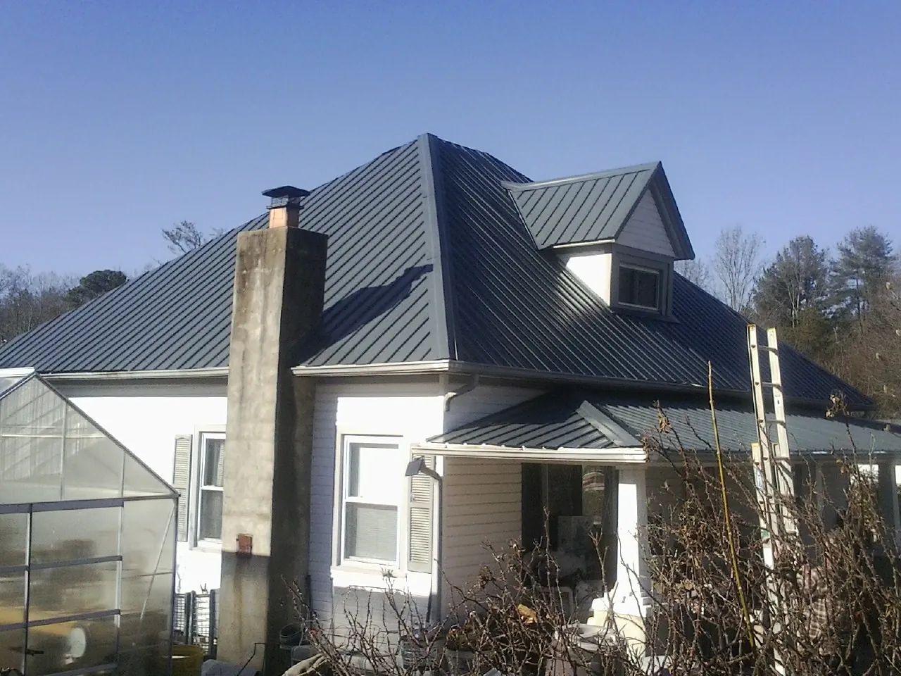 Dark blue standing seam metal roof on a white farmhouse with dormer — Slate & Tile Roof Repair by Roofing Brothers in Bunnlevel