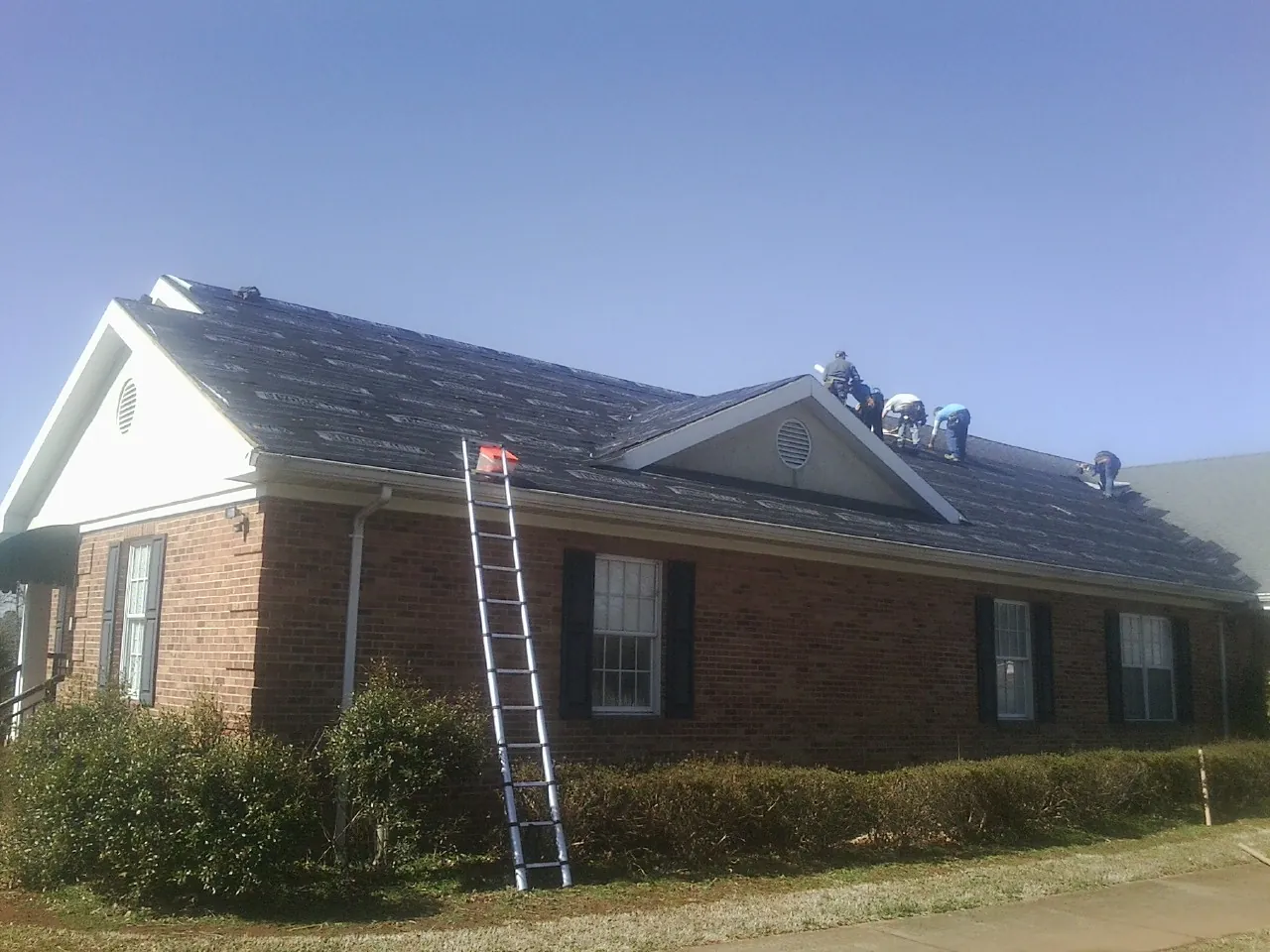 Crew tearing shingles off a brick ranch roof with a ladder set — Metal Roof Repair work by our crew in Bunnlevel
