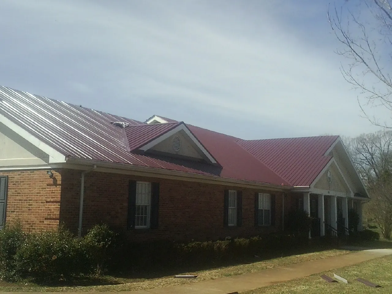 Red metal roof with gabled entries on a long brick building, from a Hail Damage Roof Repair job in Bunnlevel