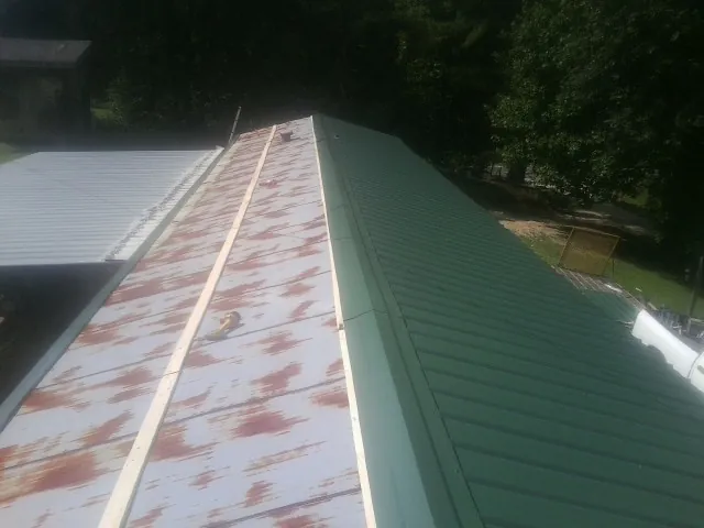 Old rusted panels beside newly installed green metal roofing — Wind Damage Roof Repair by Roofing Brothers in Bunnlevel